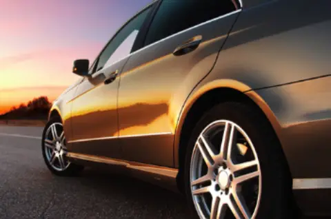 A sleek car with shiny alloy wheels parked on the road, illuminated by a vibrant sunset in the background